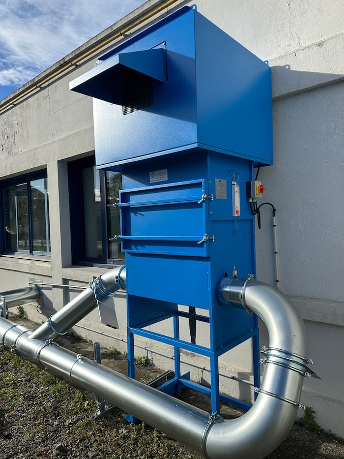 Système de filtration industriel bleu avec conduits métalliques installé contre un bâtiment blanc
